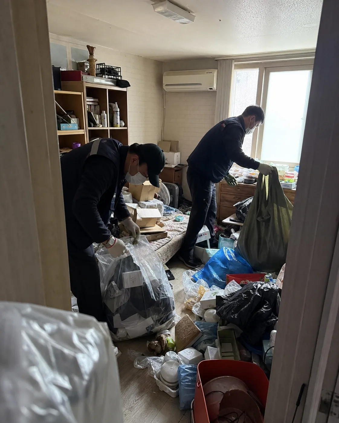 물품이 쌓인 주거공간에서 보존품과 폐기 대상을 분류해 포장하는 특수청소 작업 장면